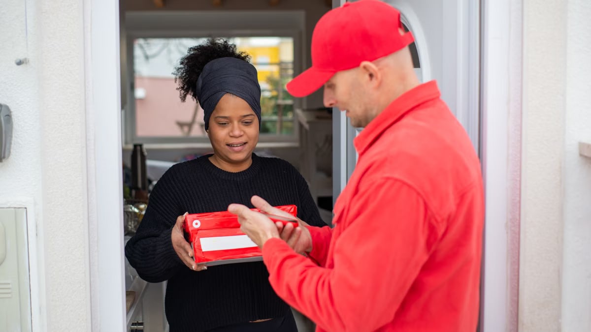 A courier hands a package to a smiling woman at her home entrance, symbolizing efficient delivery service.